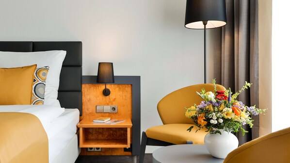 A hotel room with a bed, a nightstand with a lamp, a chair, and a vase of flowers.