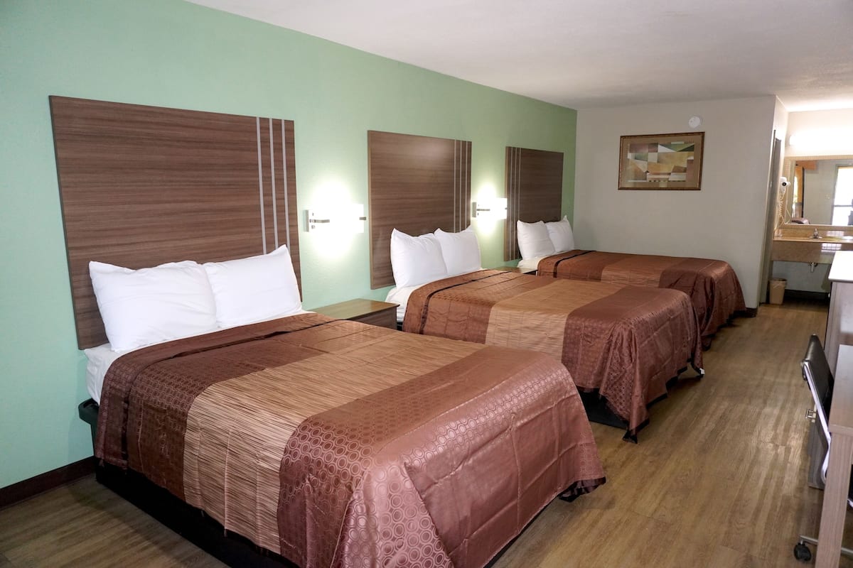 A hotel room with three beds, each with a headboard, a bedside table, and a lamp.