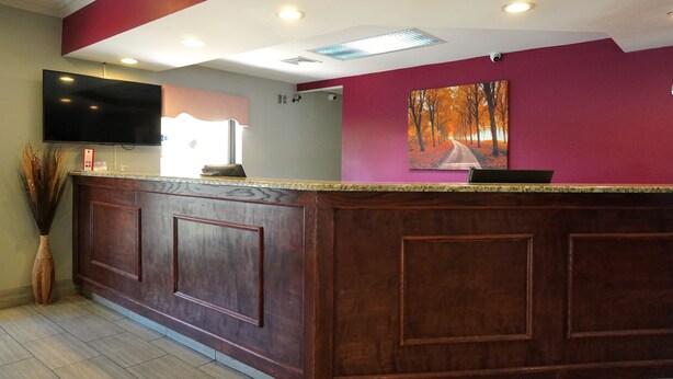A reception area with a wooden counter, a flat-screen TV, and a painting on the wall. - Fairview Inn and Suites (Mobile)