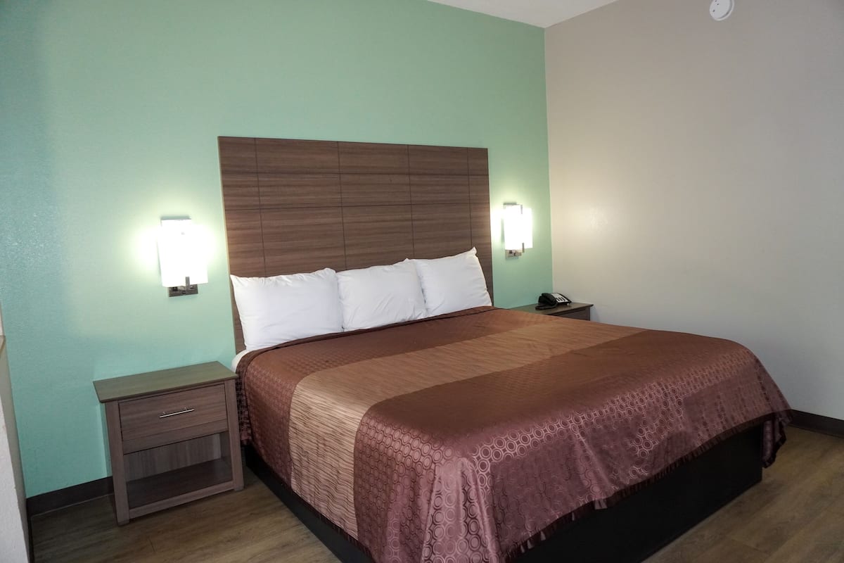 A hotel room with a bed, nightstand, and wall-mounted lamps.