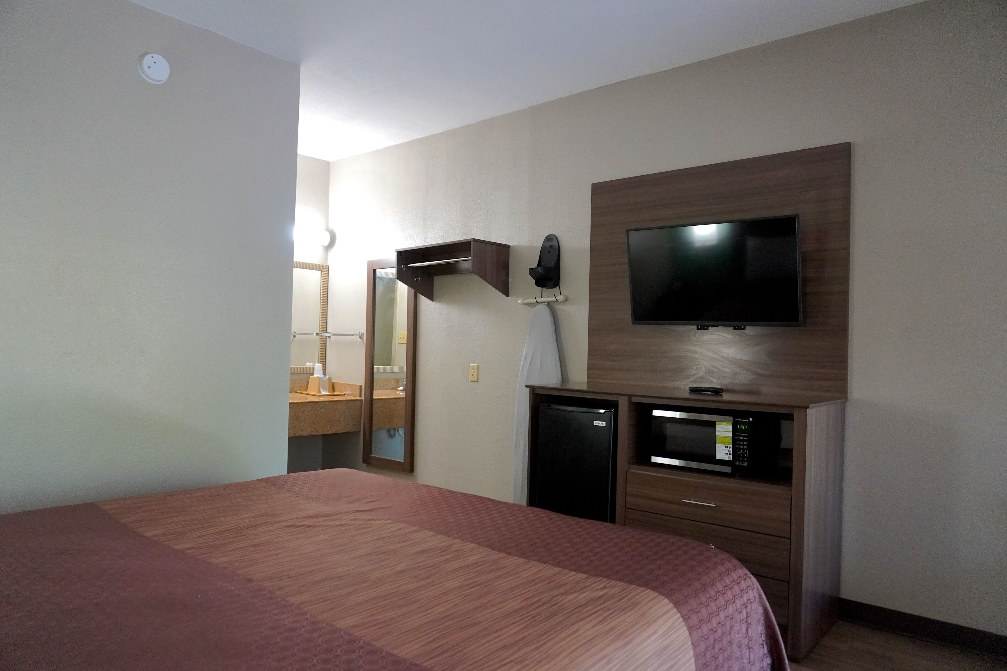 Een hotelkamer met een bed, een aan de muur bevestigde televisie, een magnetron en een kleine koelkast.