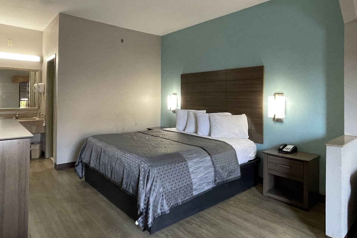 A hotel room with a bed, bedside table, lamp, and a mirror.