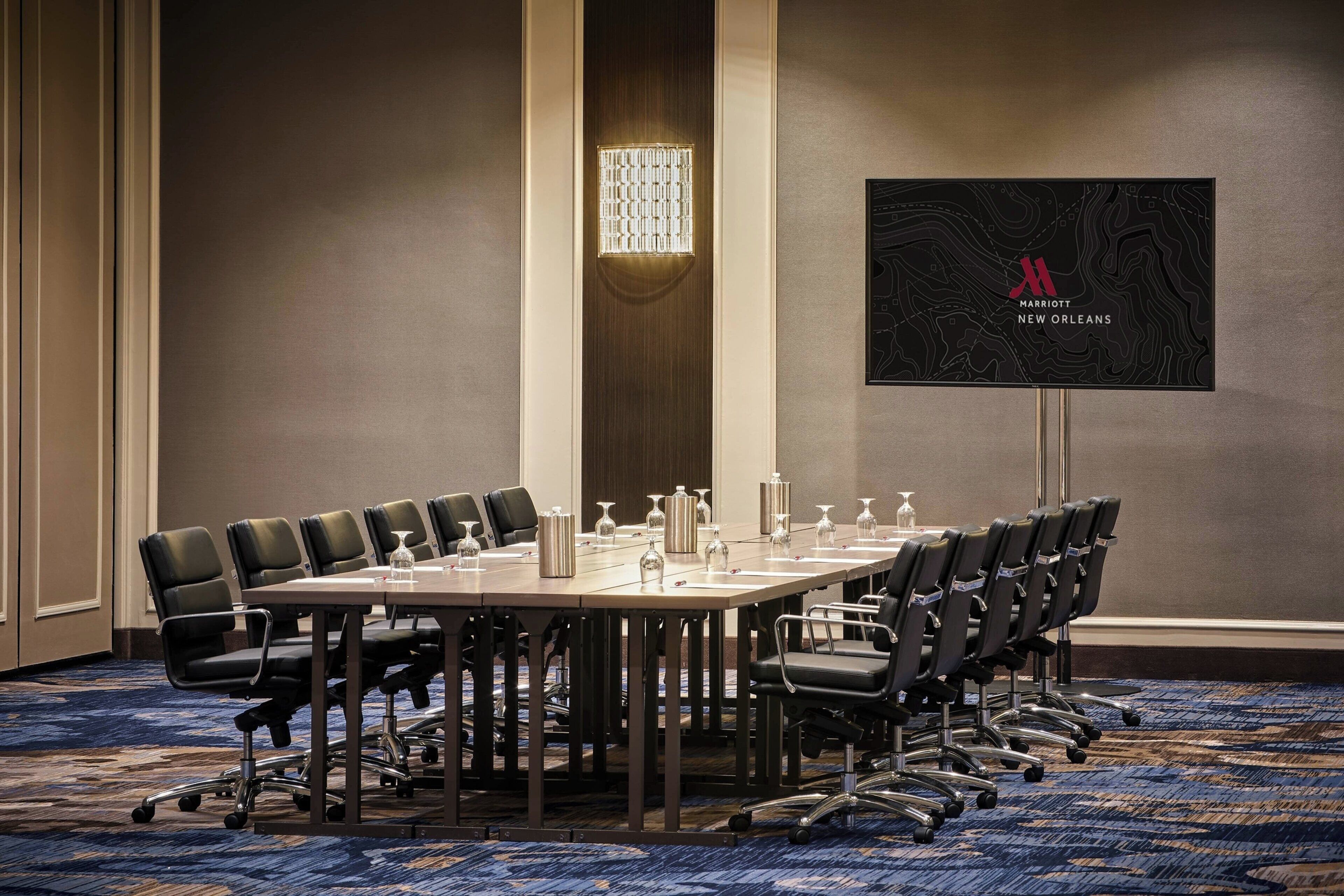 A conference room with a long table, multiple chairs, and a large screen displaying the Marriott New Orleans logo.