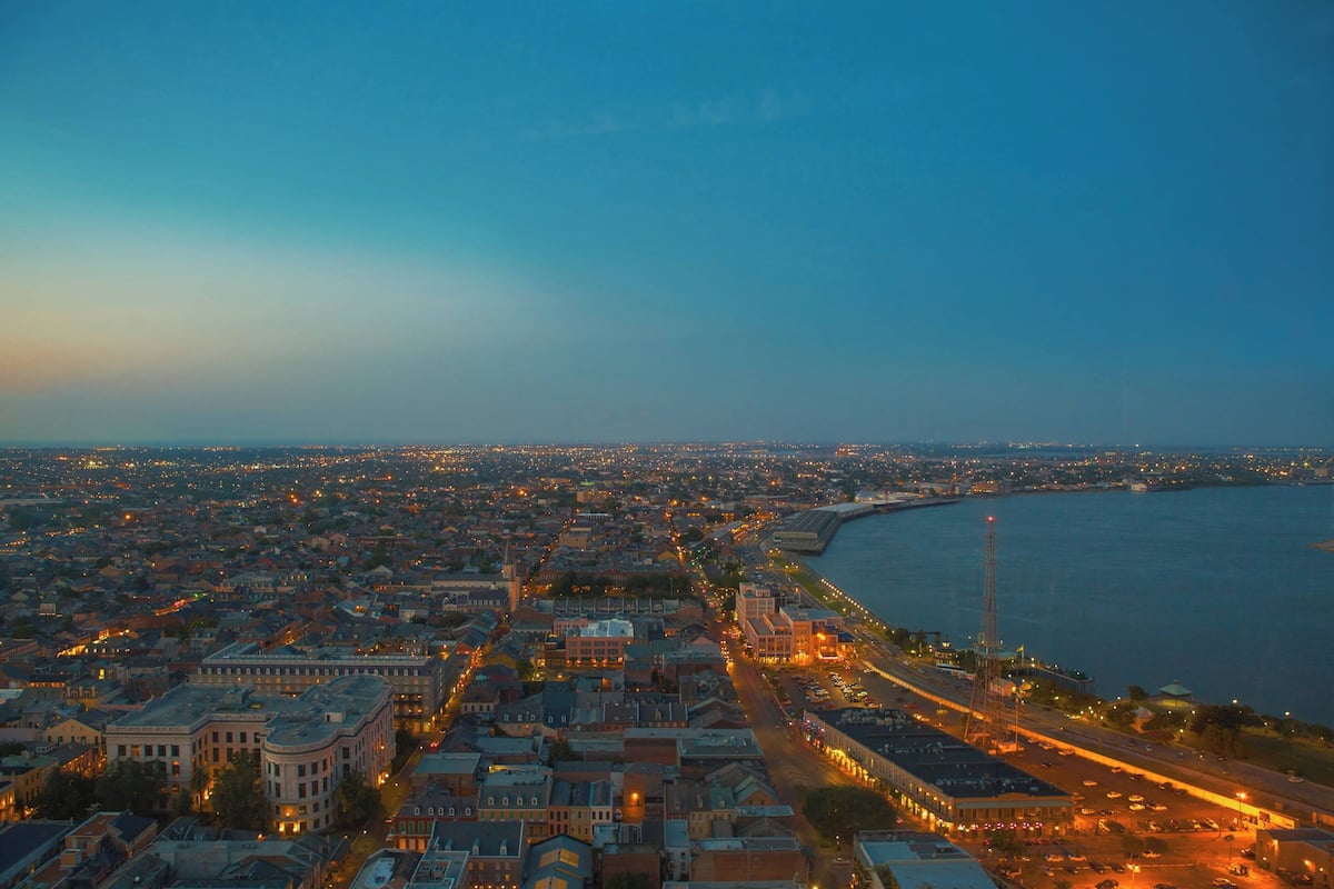 An aerial view of a cityscape at dusk with a prominent waterfront, dense urban buildings, and a clear sky.