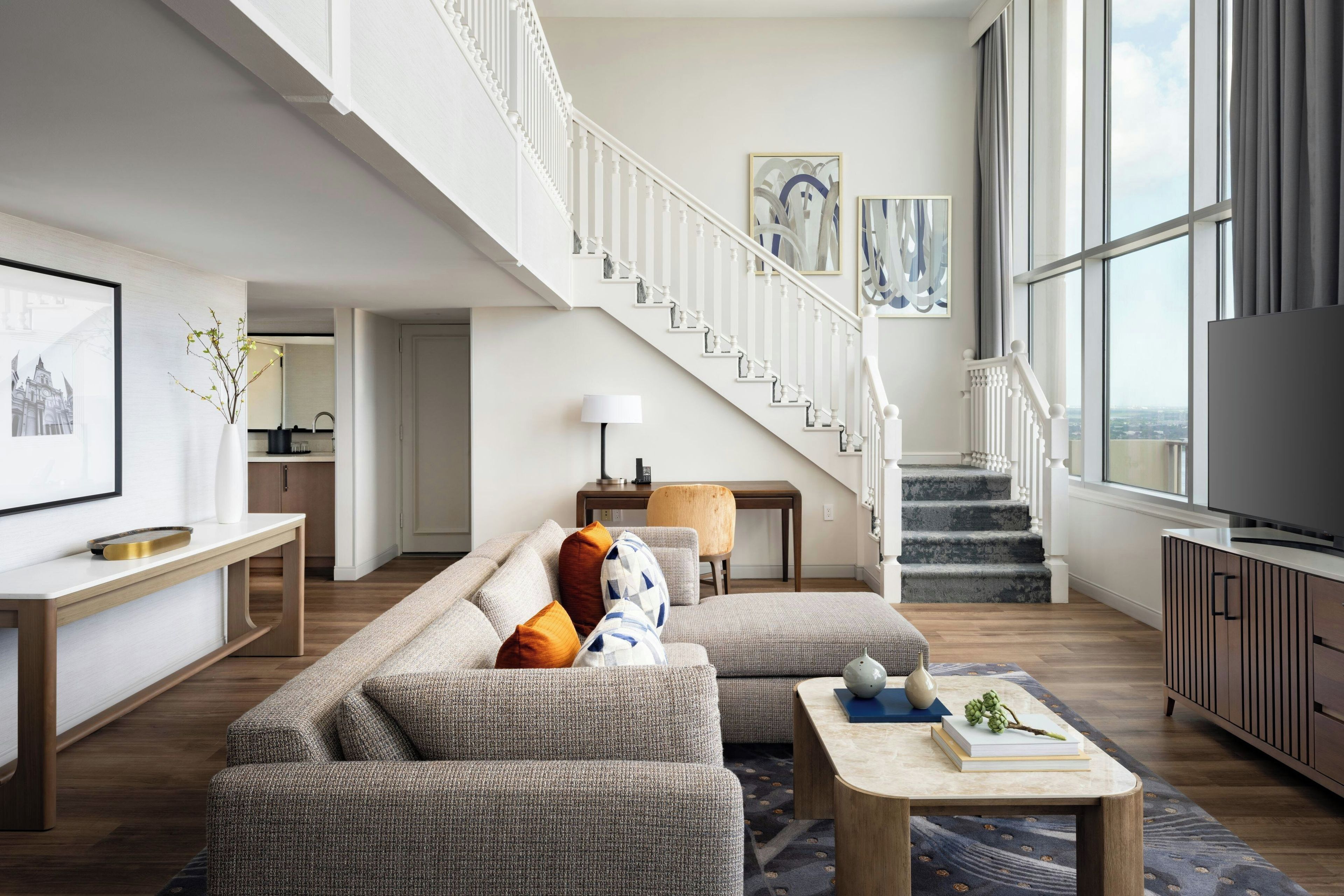 A modern living room with a staircase, a sofa set, a coffee table, and a television.