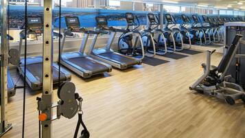 Un gimnasio con cintas de correr, máquinas de pesas y vistas de la ciudad.