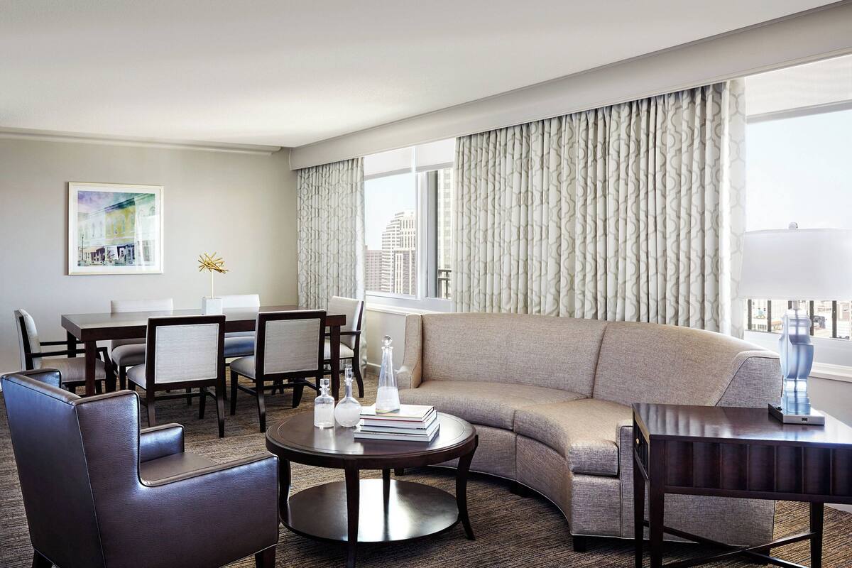A modern hotel room with a sofa, armchairs, a dining table, and a coffee table.