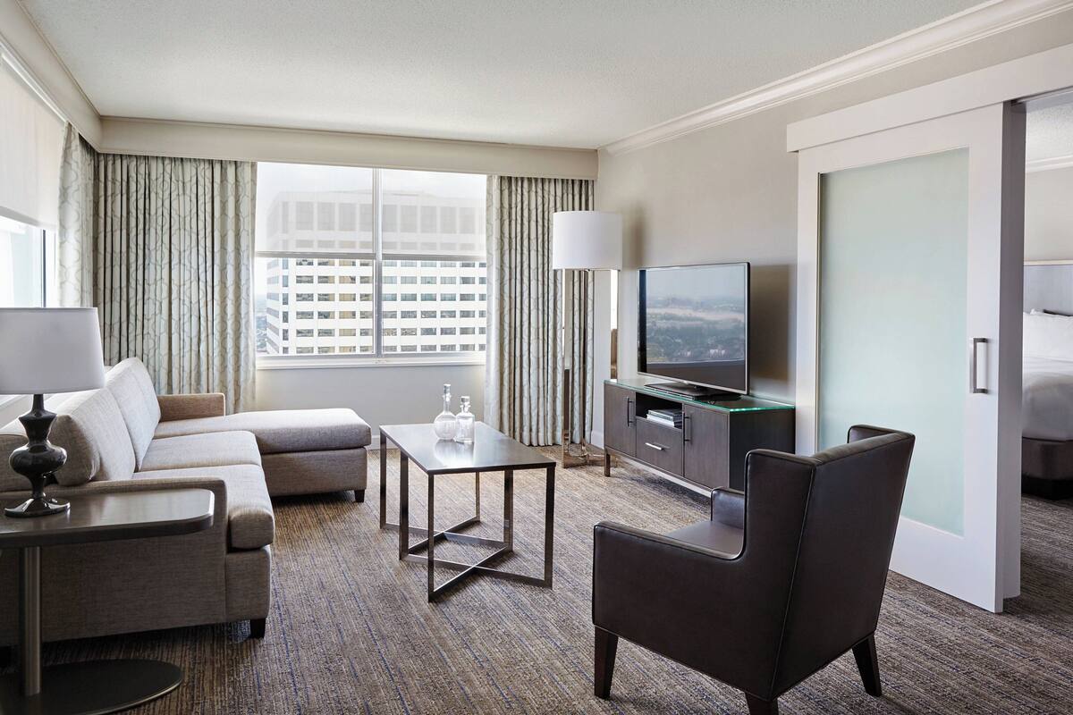 A modern hotel room with a sofa, a small table, a chair, a television, and a minibar.
