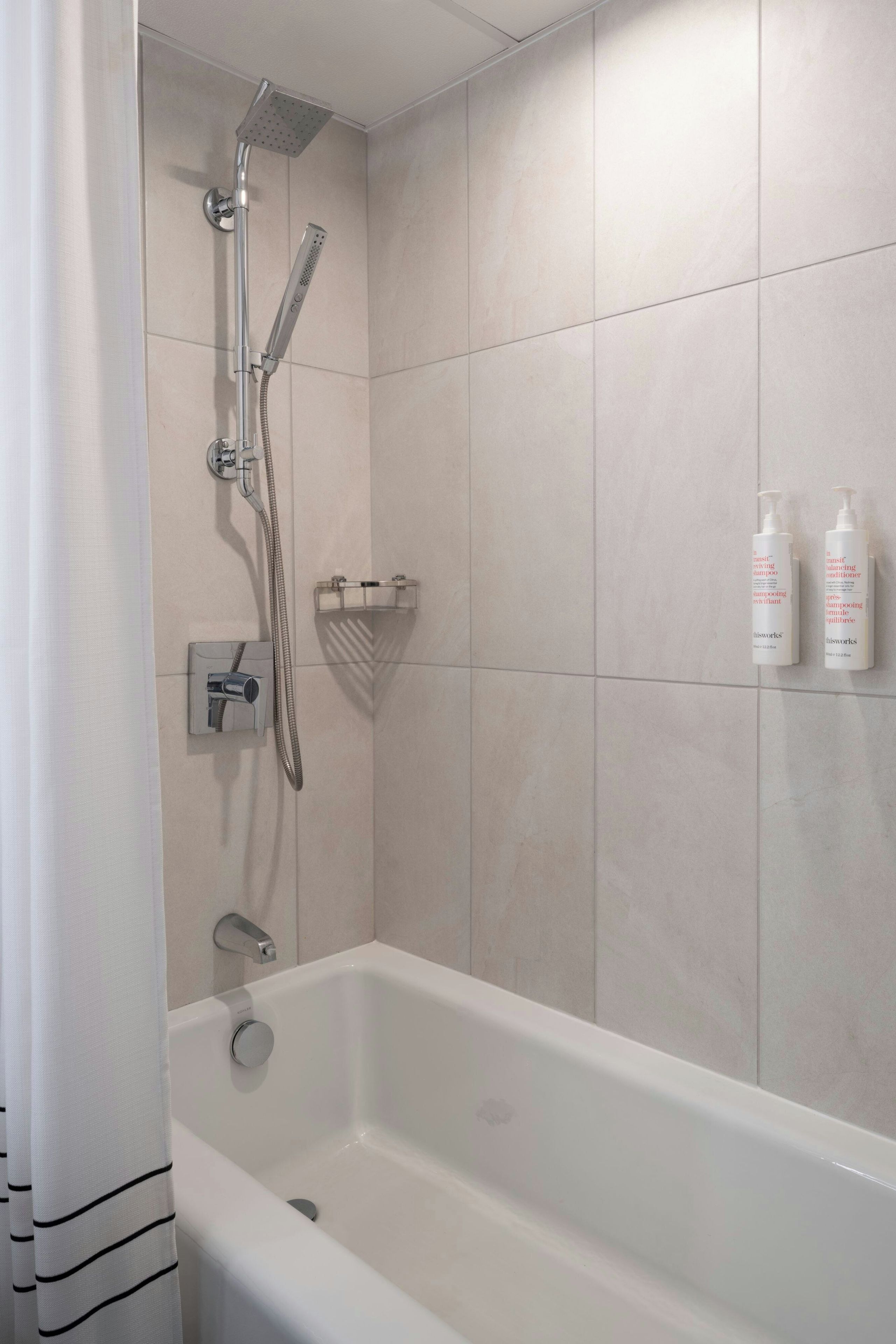 Un baño moderno con bañera, ducha y dos botellas de champú en la pared.