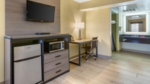 A hotel room with a kitchenette, a flat-screen TV mounted on the wall, a desk with a chair, and a large mirror. - SureStay by Best Western Chambers Petrified Forest (Chambers)