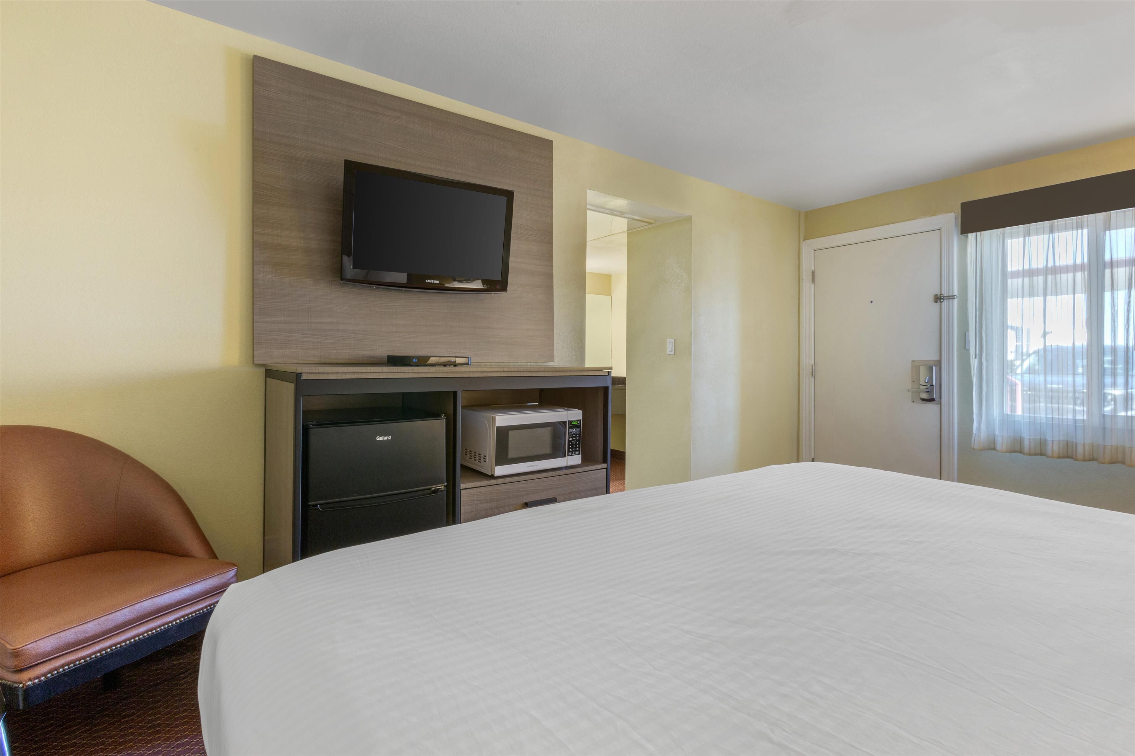 Een hotelkamer met een bed, een aan de muur bevestigde televisie, een magnetron en een stoel.