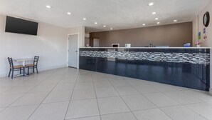 A reception area with a black counter, a small table with chairs, and a wall-mounted TV. - SureStay by Best Western Chambers Petrified Forest (Chambers)