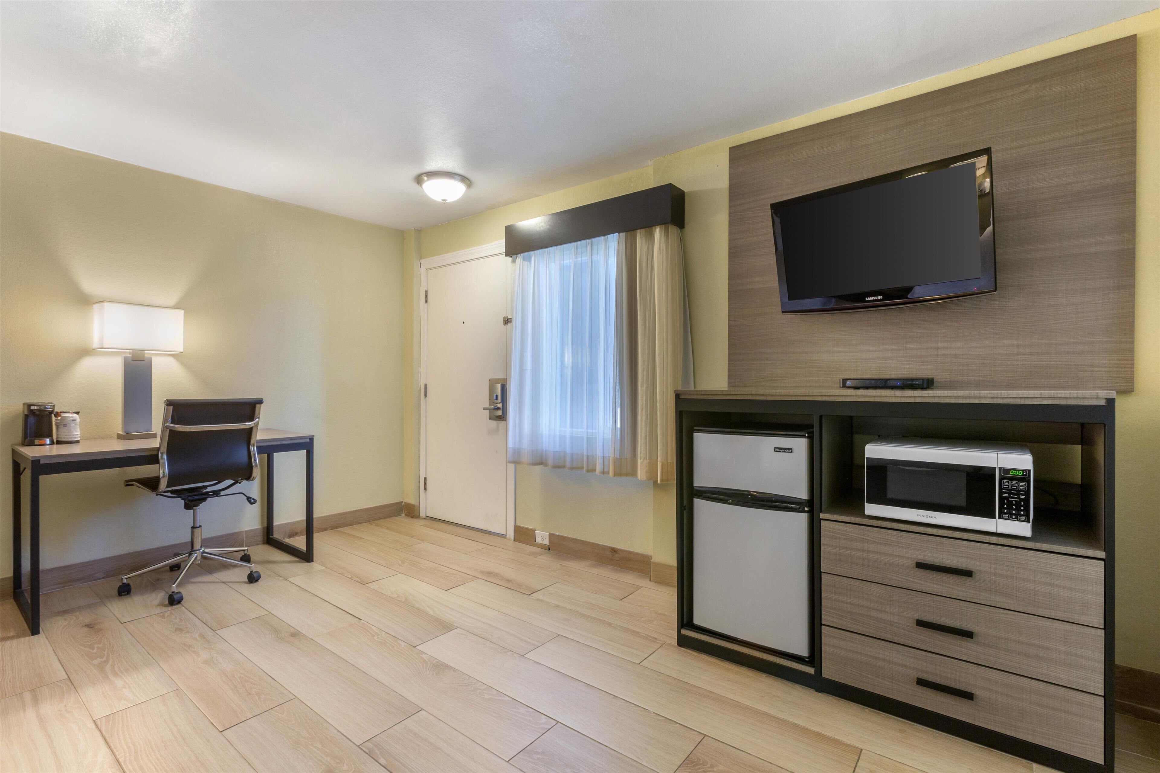 Une chambre d’hôtel équipée d’un bureau, d’une chaise, d’une télévision, d’un four à micro-ondes et d’un petit réfrigérateur.