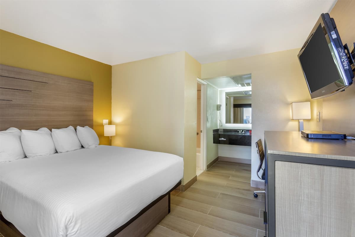 A hotel room with a bed, bedside lamps, a desk with a flat-screen TV, and a mirror.