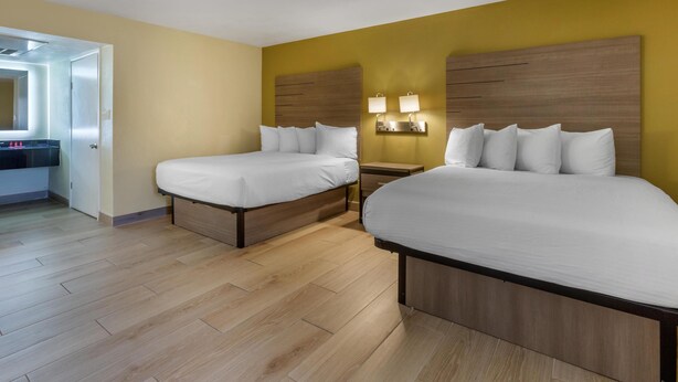 A hotel room with two beds, wooden headboards, a nightstand with lamps, and a mirror above the door. - SureStay by Best Western Chambers Petrified Forest (Chambers)