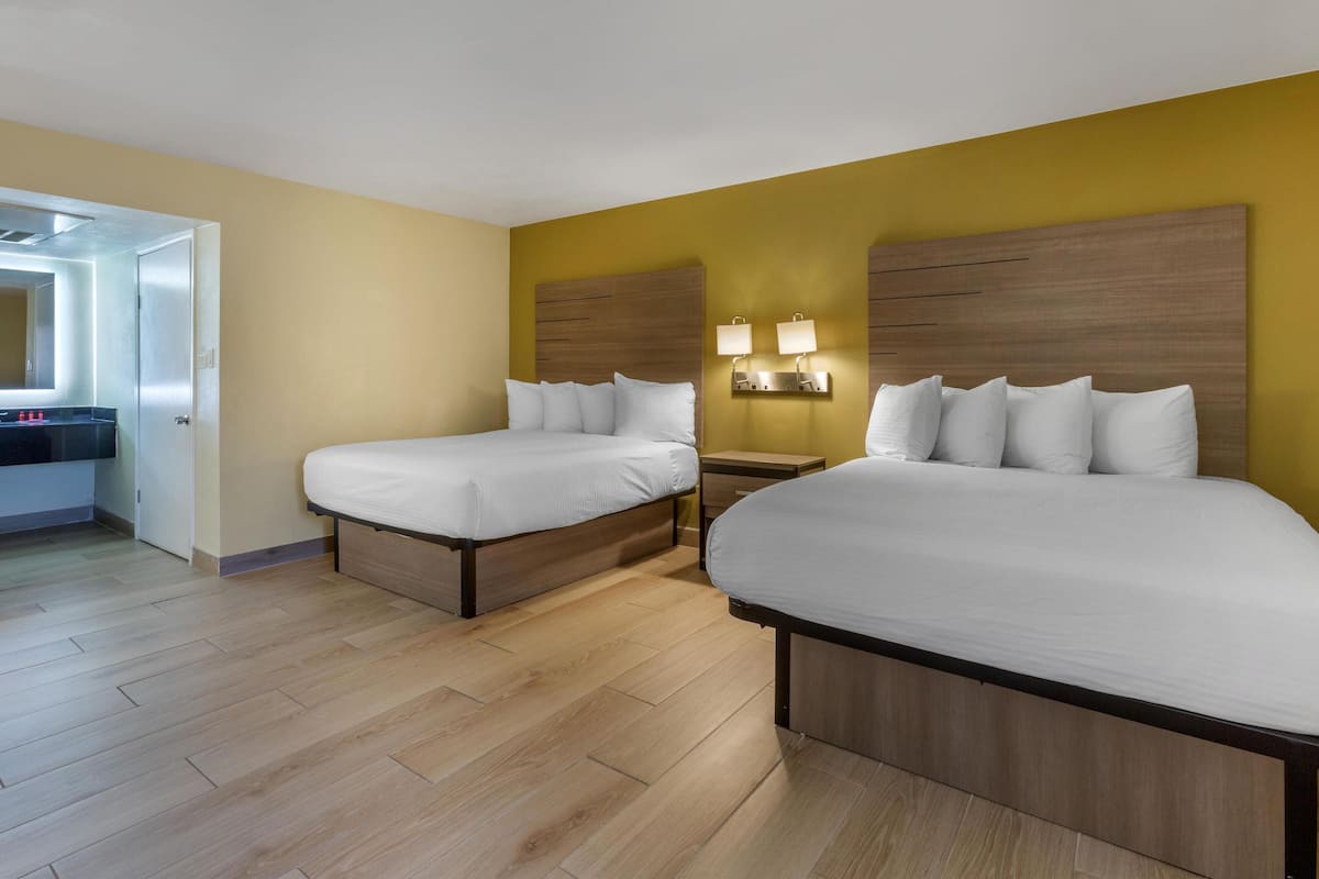 A hotel room with two beds, wooden headboards, a nightstand with lamps, and a mirror above the door.