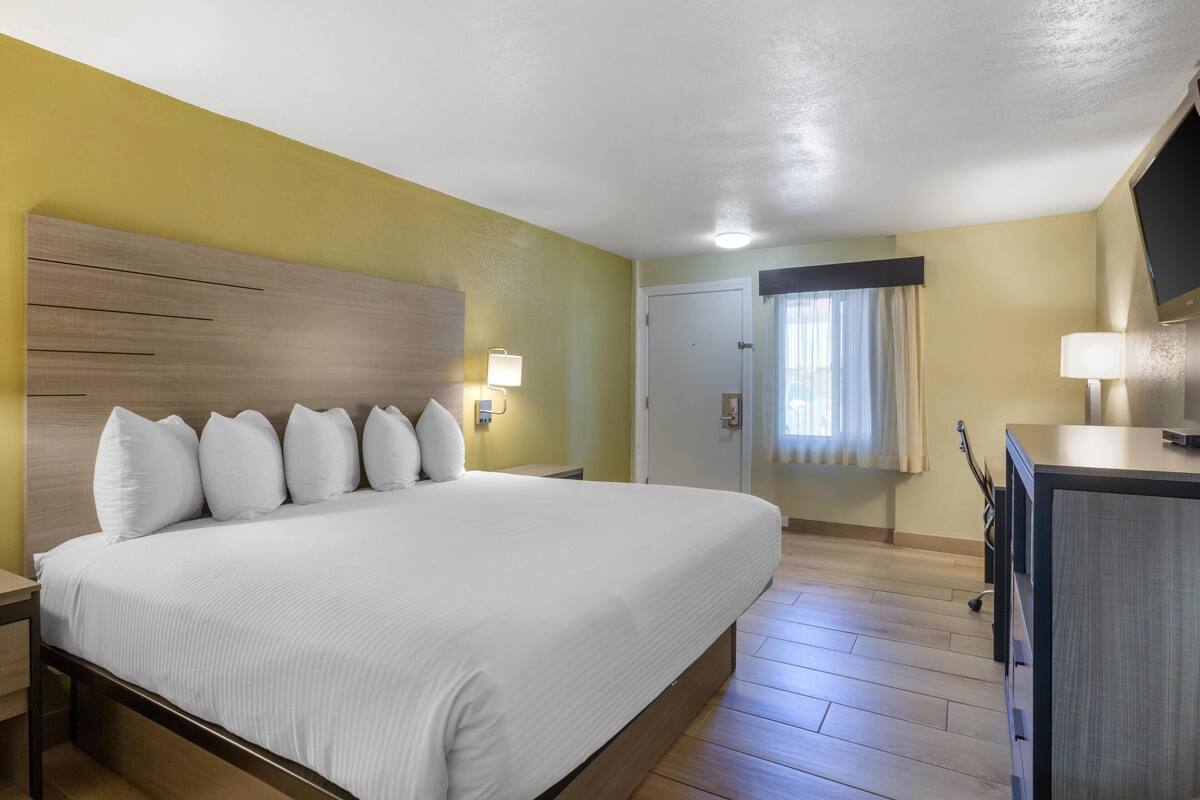 A hotel room with a large bed, bedside lamps, a wooden headboard, a desk with a lamp, and a television.