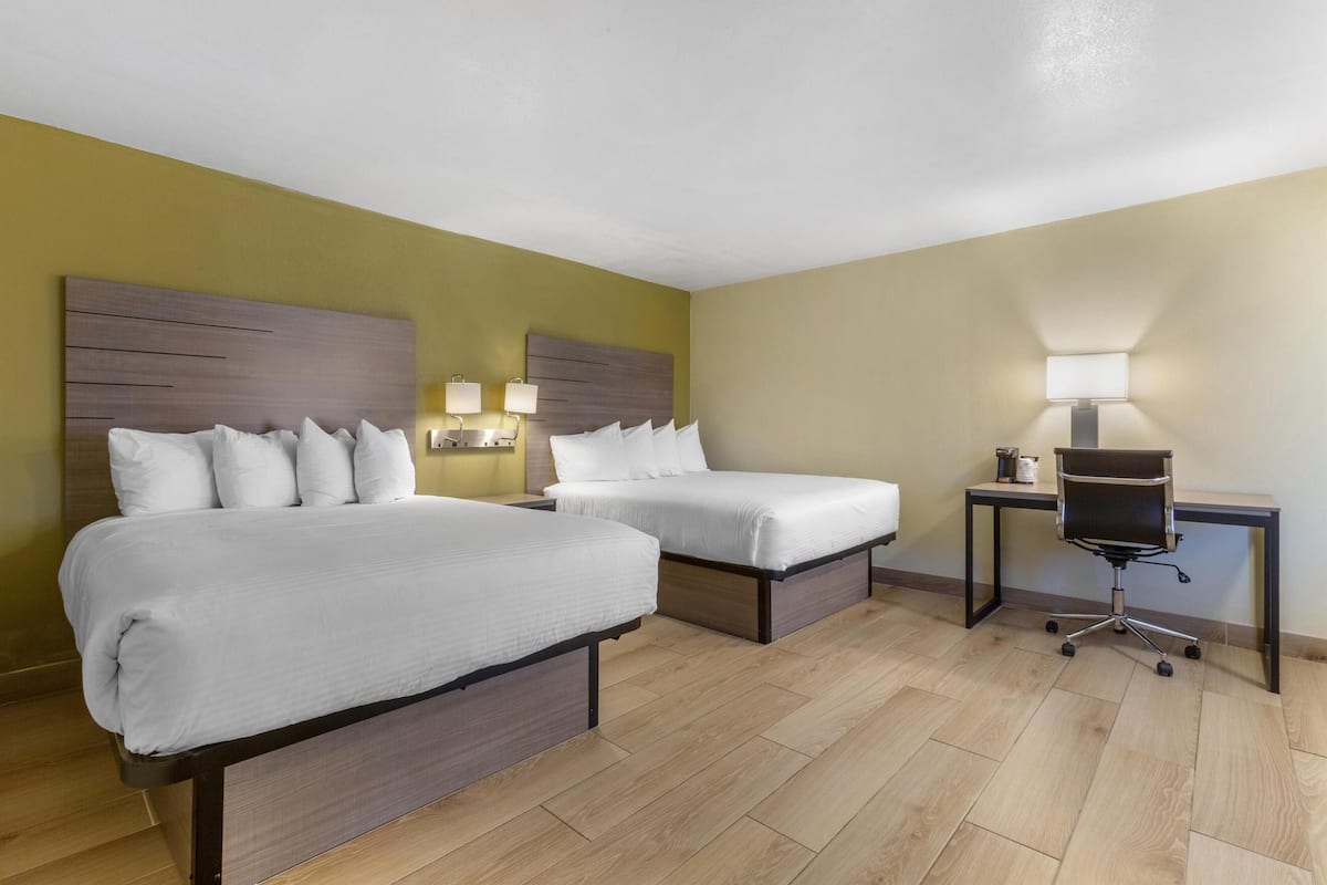 A hotel room with two beds, a desk, and a chair.