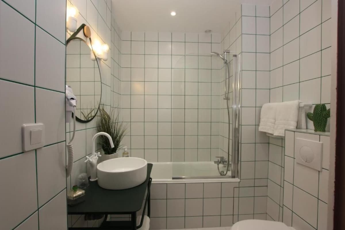 A compact bathroom with a round sink, a glass shower enclosure, and a white bathtub.
