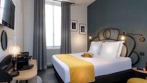 Habitación de hotel con cama, escritorio, silla, televisor y ventana con cortinas.