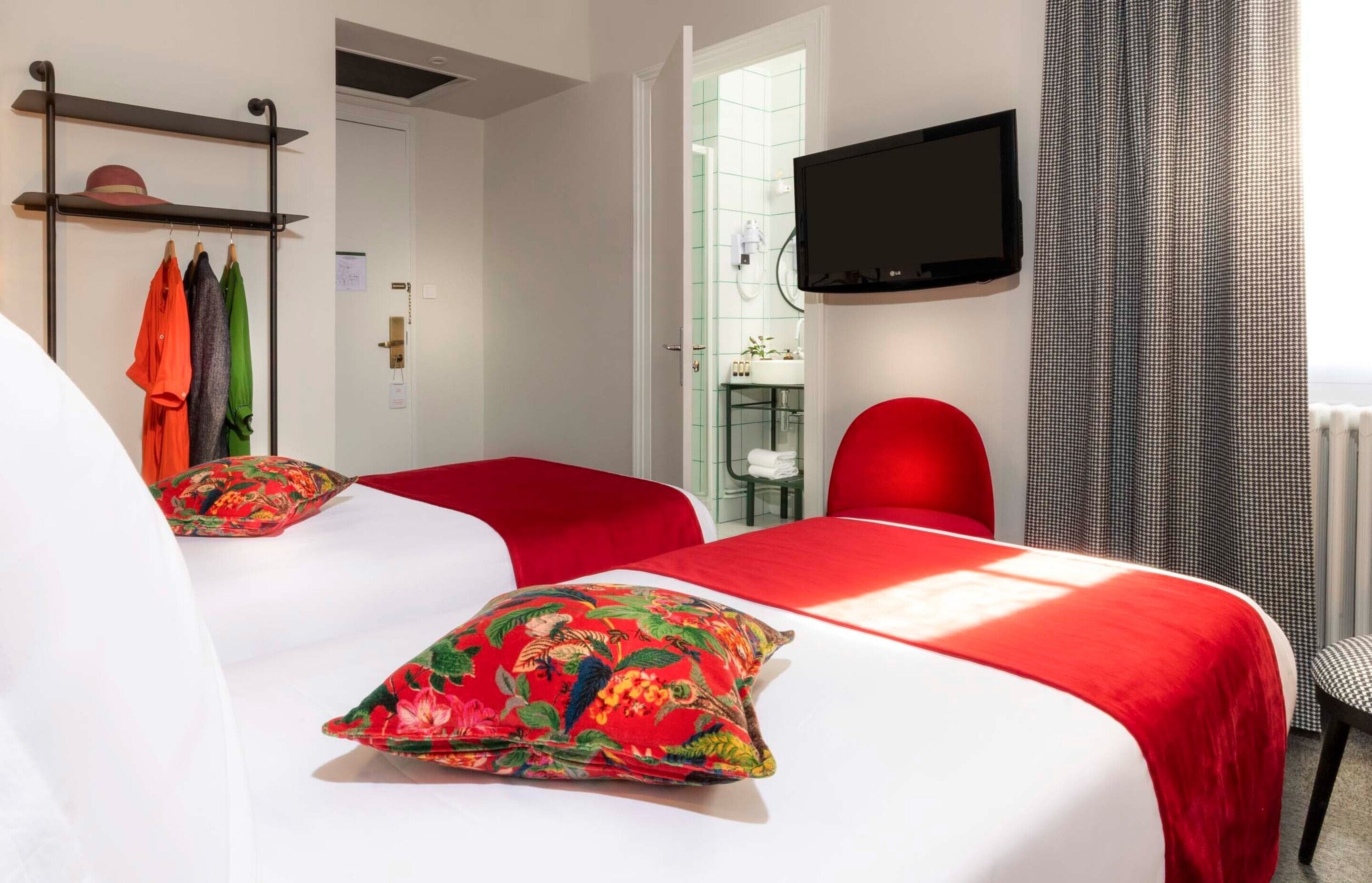 A hotel room with two beds, a TV mounted on the wall, and a red chair.