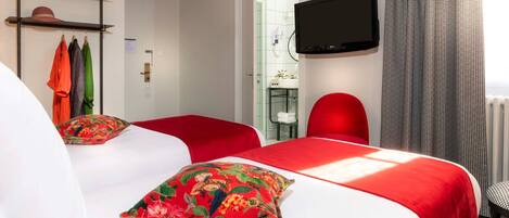 Una habitación de hotel con dos camas, un televisor montado en la pared y una silla roja.