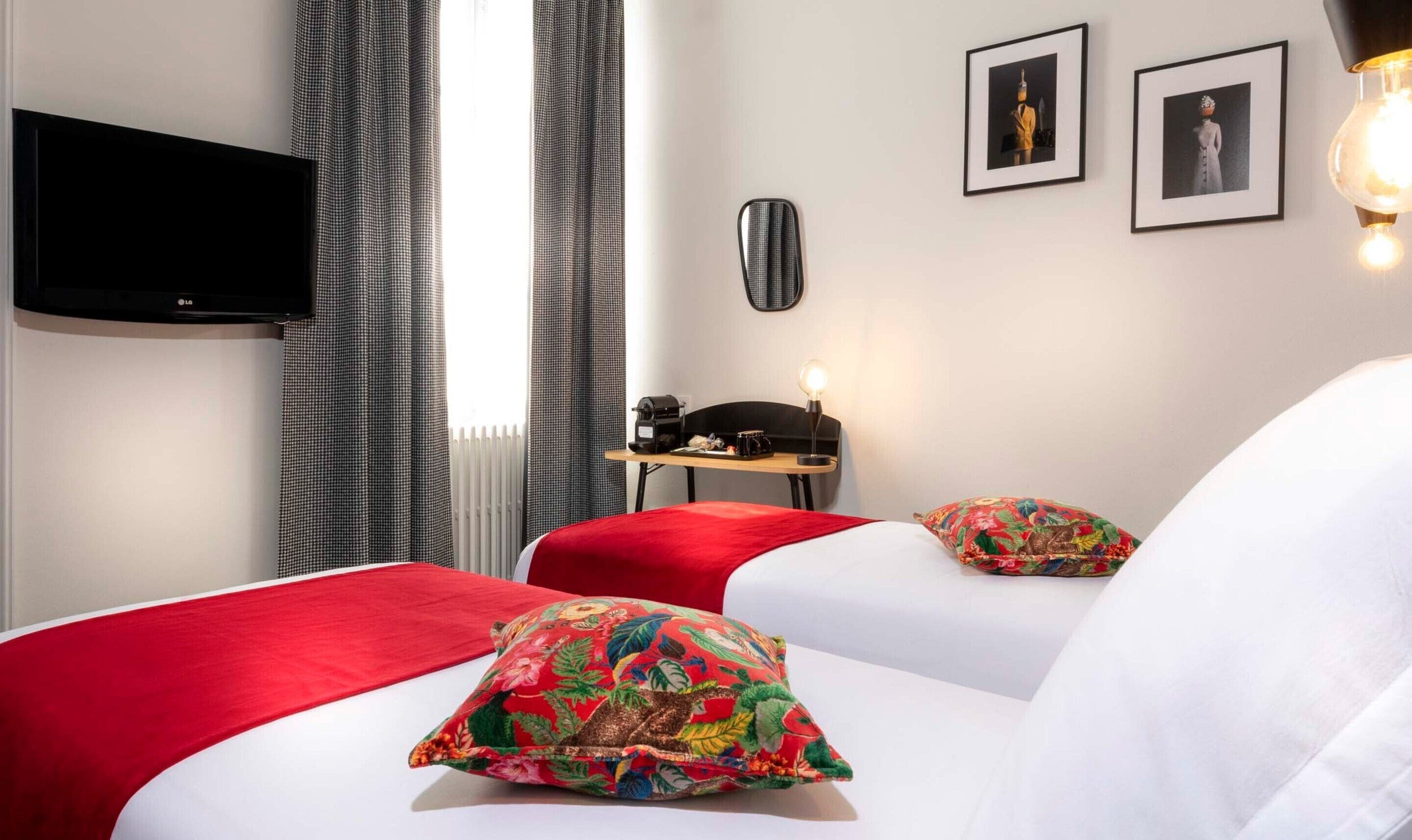 A hotel room with a bed, a desk, a chair, a television, and two framed pictures on the wall.