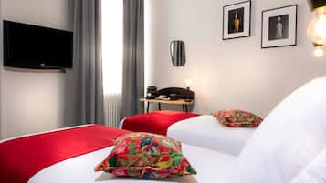 A hotel room with a bed, a desk, a chair, a television, and two framed pictures on the wall.