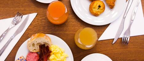 A breakfast table with plates of food, including eggs, bacon, ham, cheese, croissants, and juice. There are also two cups of coffee and a glass of orange juice.