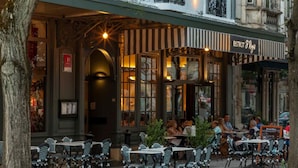 Un café al aire libre con mesas y sillas, un letrero que dice "BISTROT St Regis", y la fachada de un edificio con detalles decorativos.