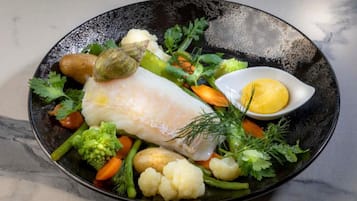 A plate of fish fillet with vegetables and a small bowl of sauce.