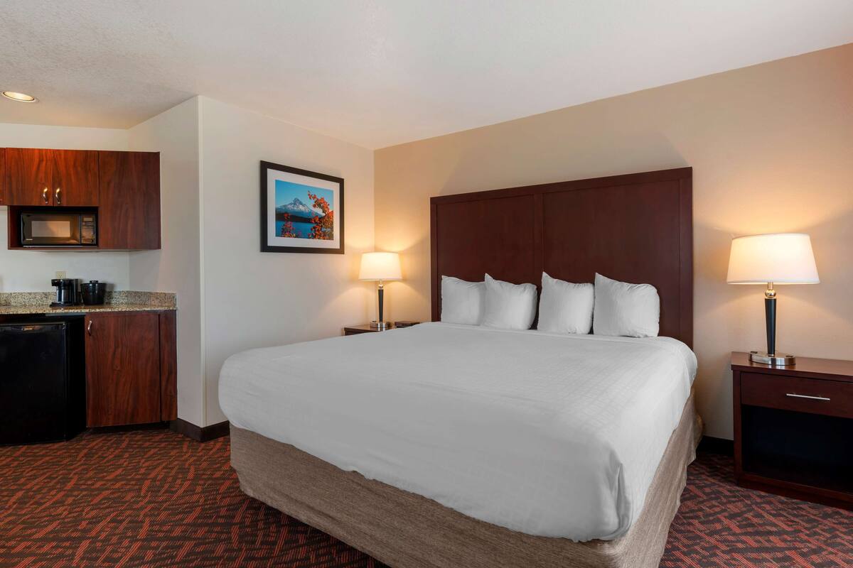 A hotel room with a large bed, a desk with a microwave, a small refrigerator, and a framed picture on the wall.