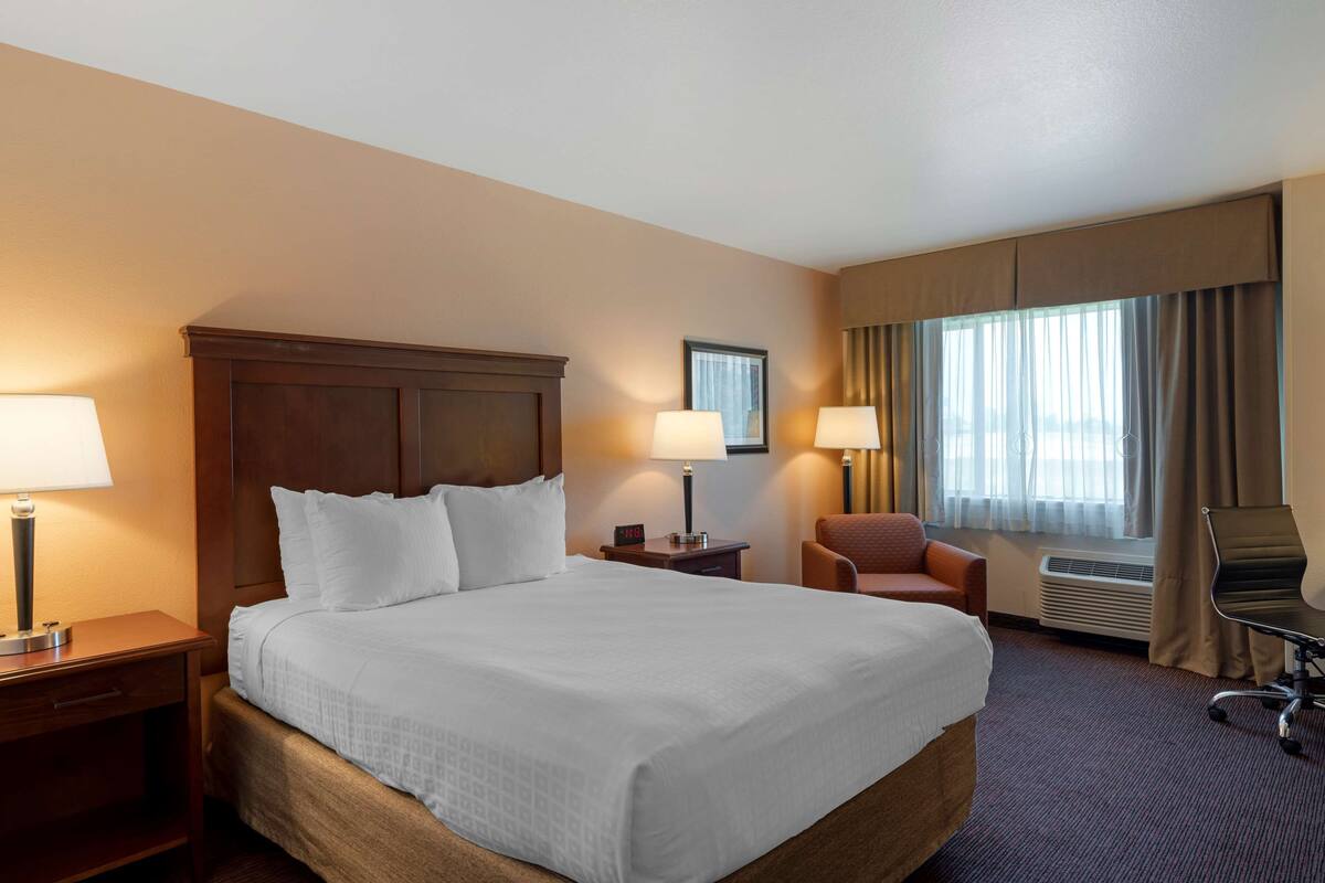 A hotel room with a large bed, two bedside tables with lamps, a chair, and a desk with a chair.