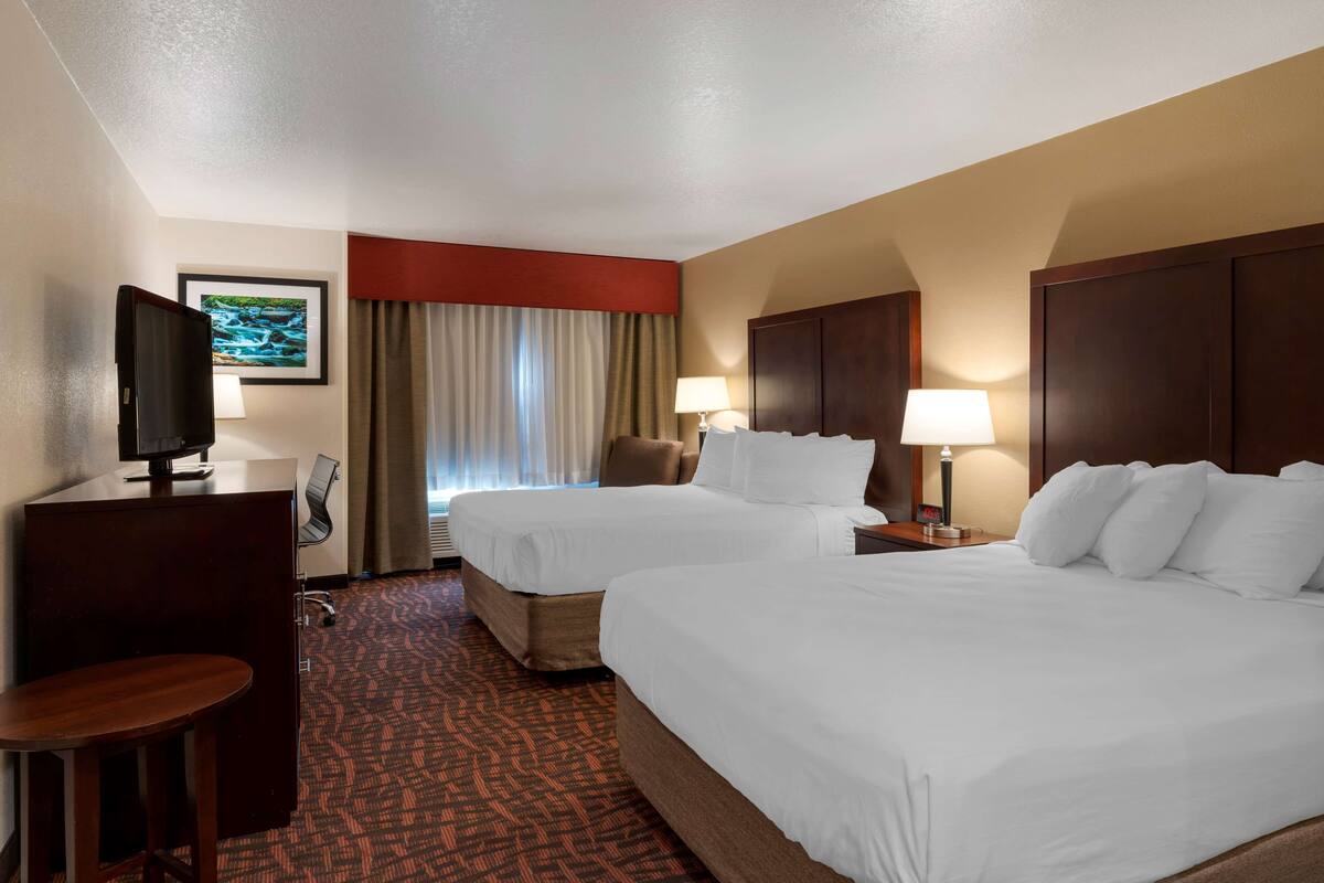 A hotel room with two beds, a desk, a TV, and a window with curtains.
