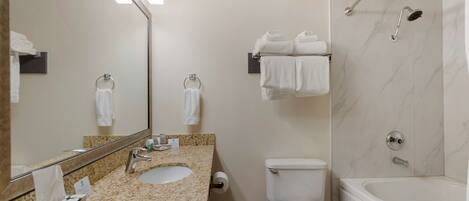 A bathroom with a granite countertop sink, a toilet, a bathtub, and a shower with a glass door.