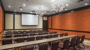 A conference room with a long table, chairs, a projector screen, and a patterned carpet.