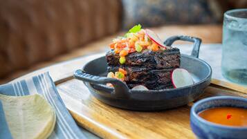 Bife com legumes em uma frigideira de ferro fundido, uma tigela de molho e um guardanapo sobre uma mesa de madeira.