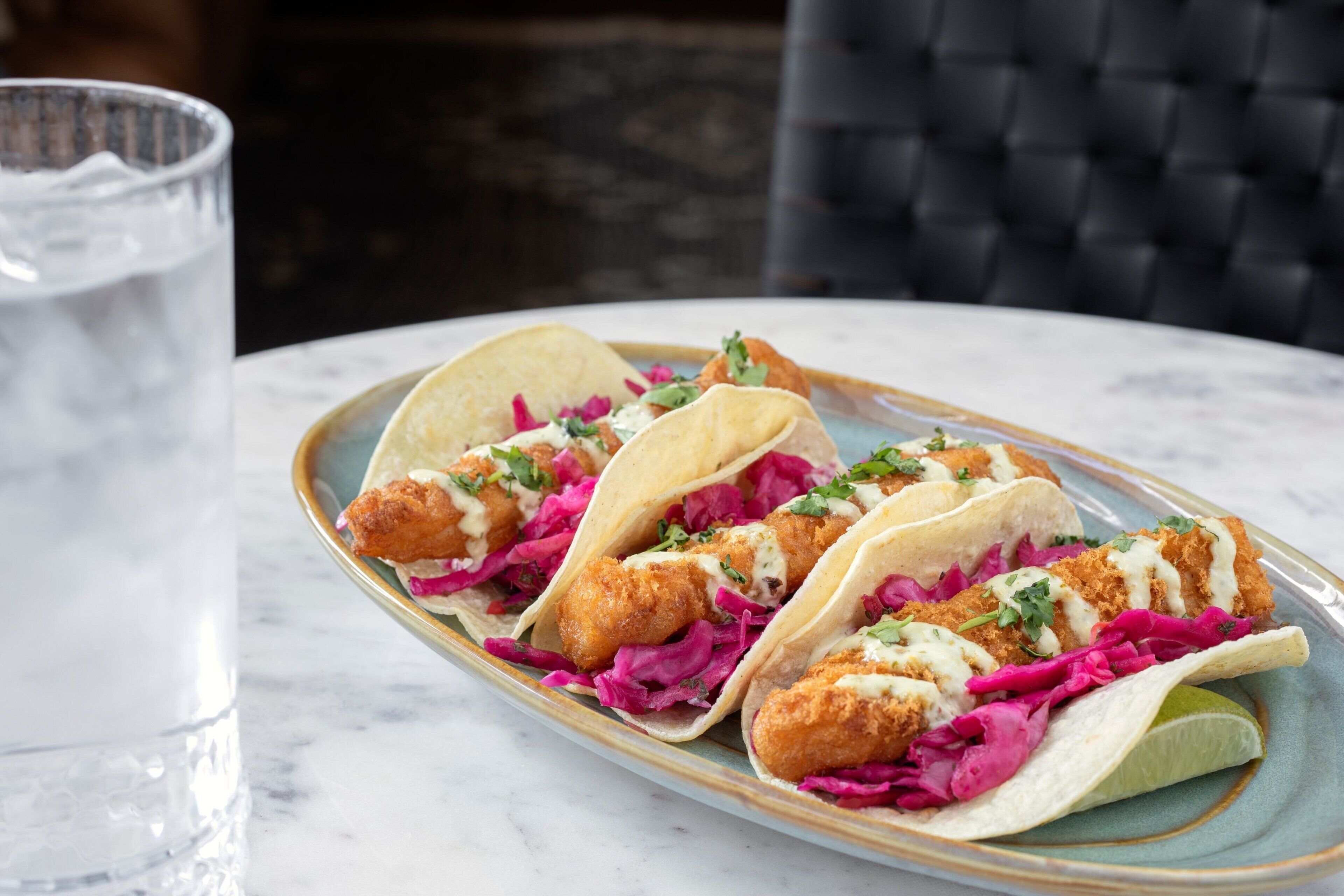 Three tacos with a lime wedge on a plate.