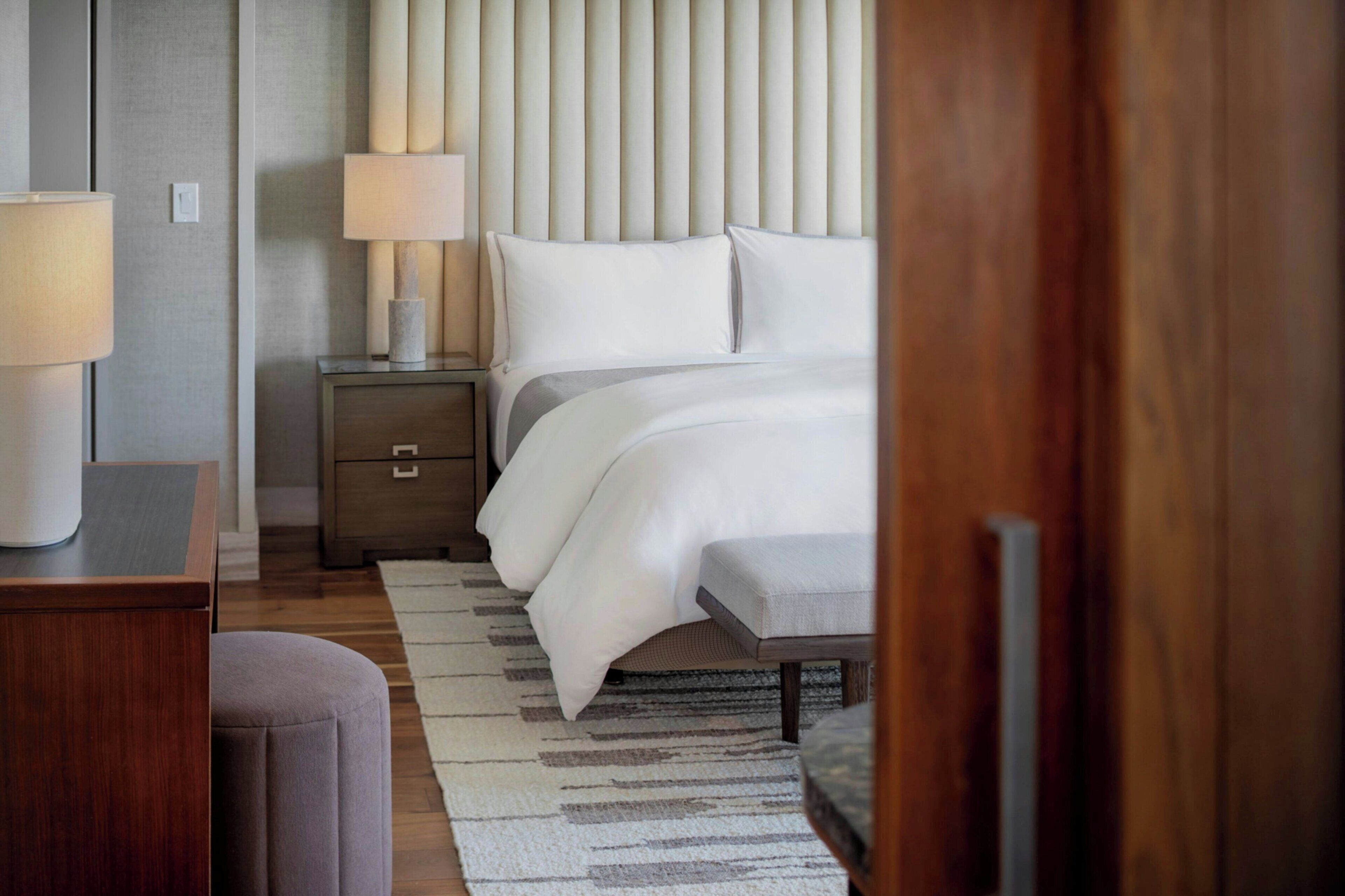A hotel room with a bed, bedside tables, a lamp, a chair, and a rug.