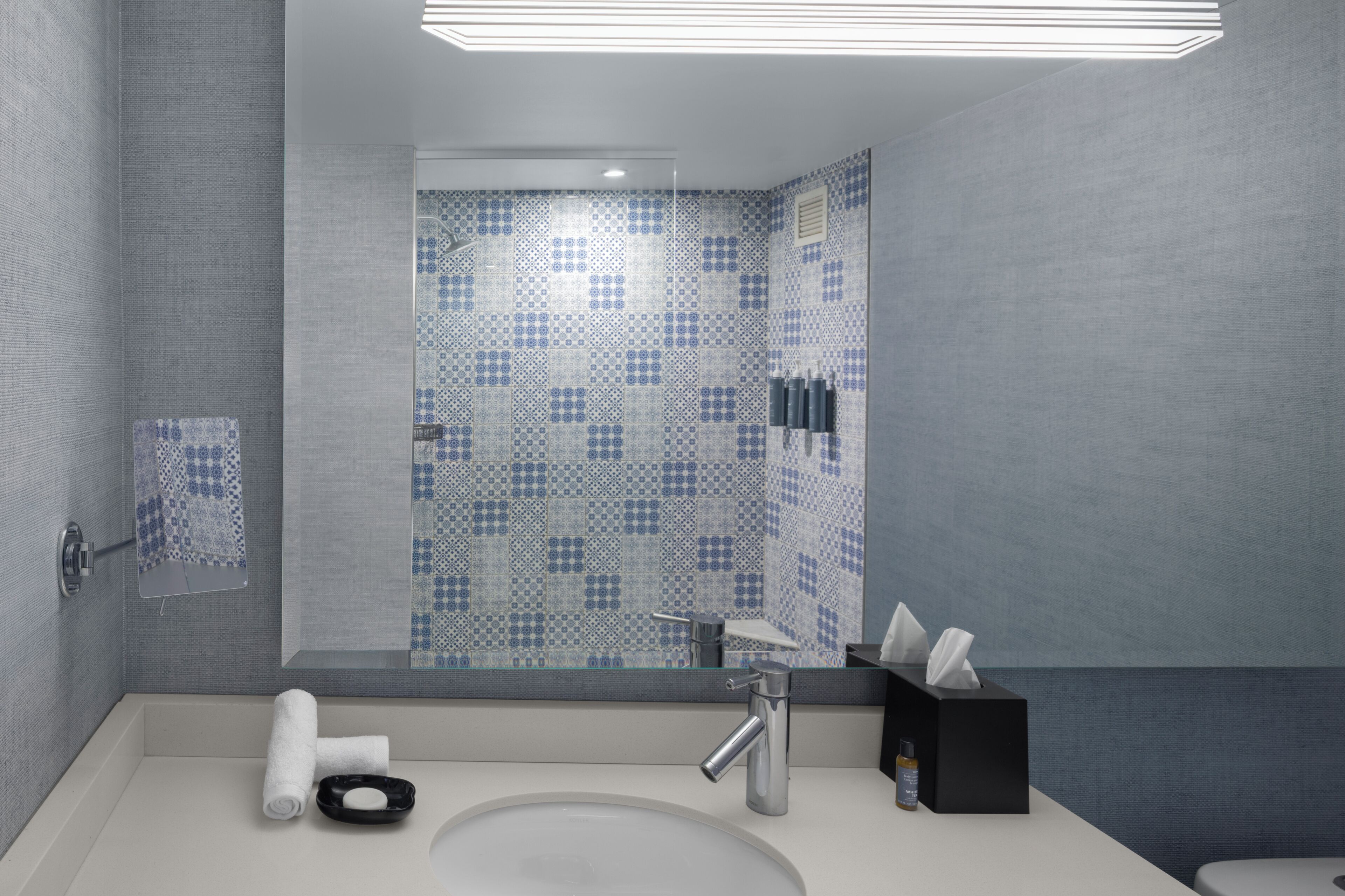 Une salle de bain moderne avec un grand miroir, un lavabo et un espace douche.