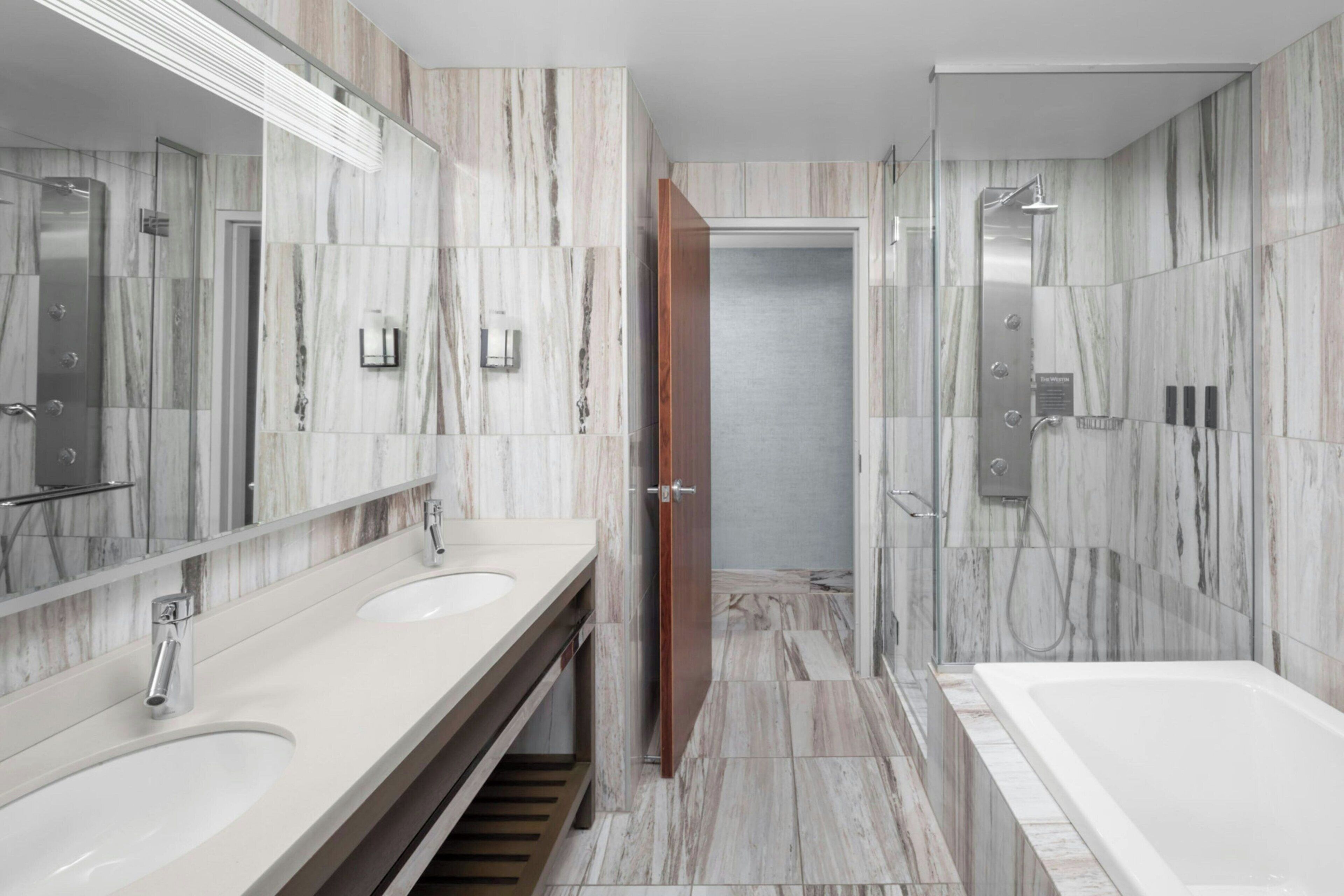 A modern bathroom with marble walls, a double sink vanity, a shower area, and a bathtub.