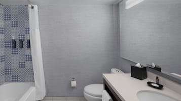 A modern bathroom with a grey tiled wall, a white toilet, a bathtub, and a vanity with a mirror.