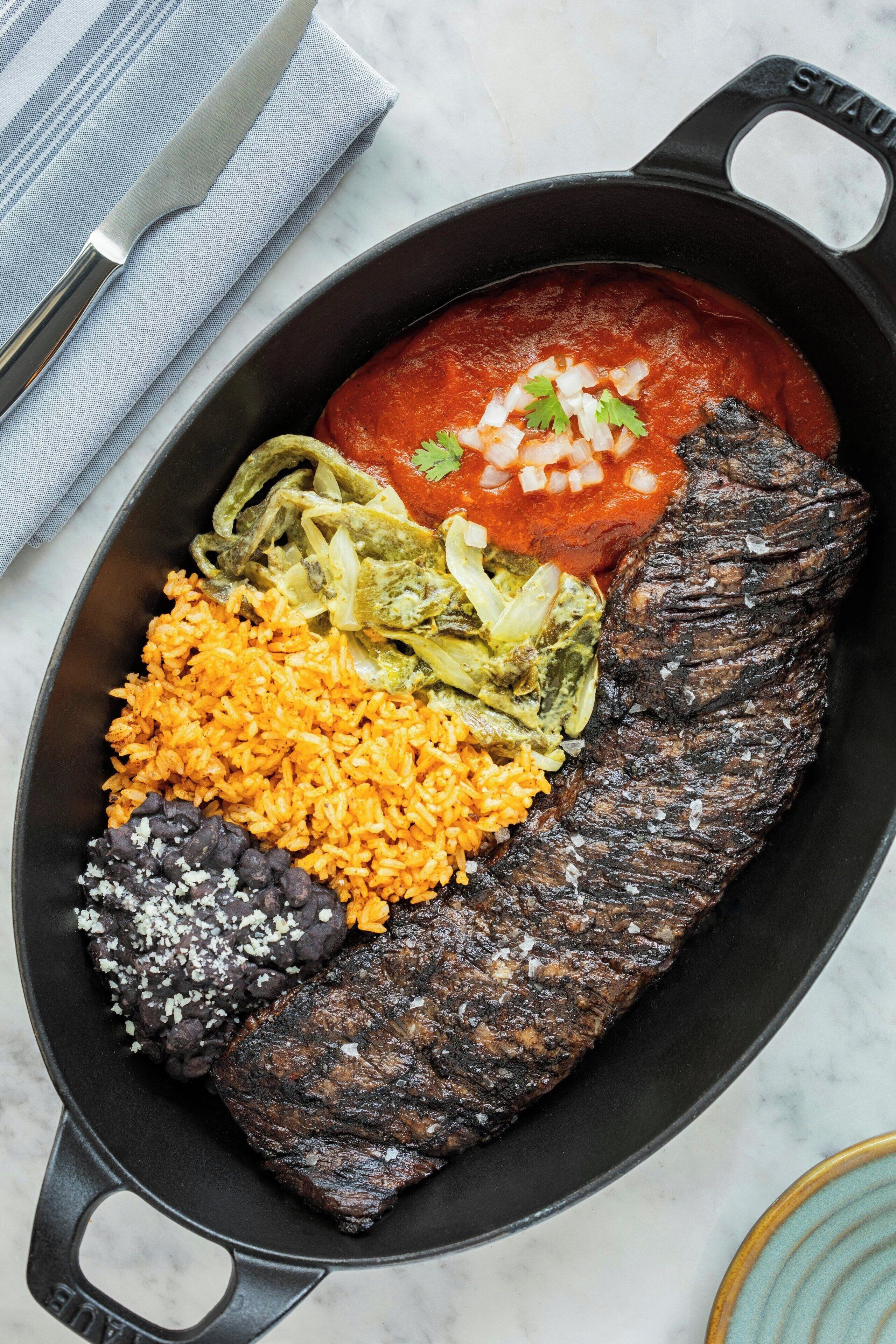 Een koekenpan met een steak, rijst, bonen en gepureerde bonen.