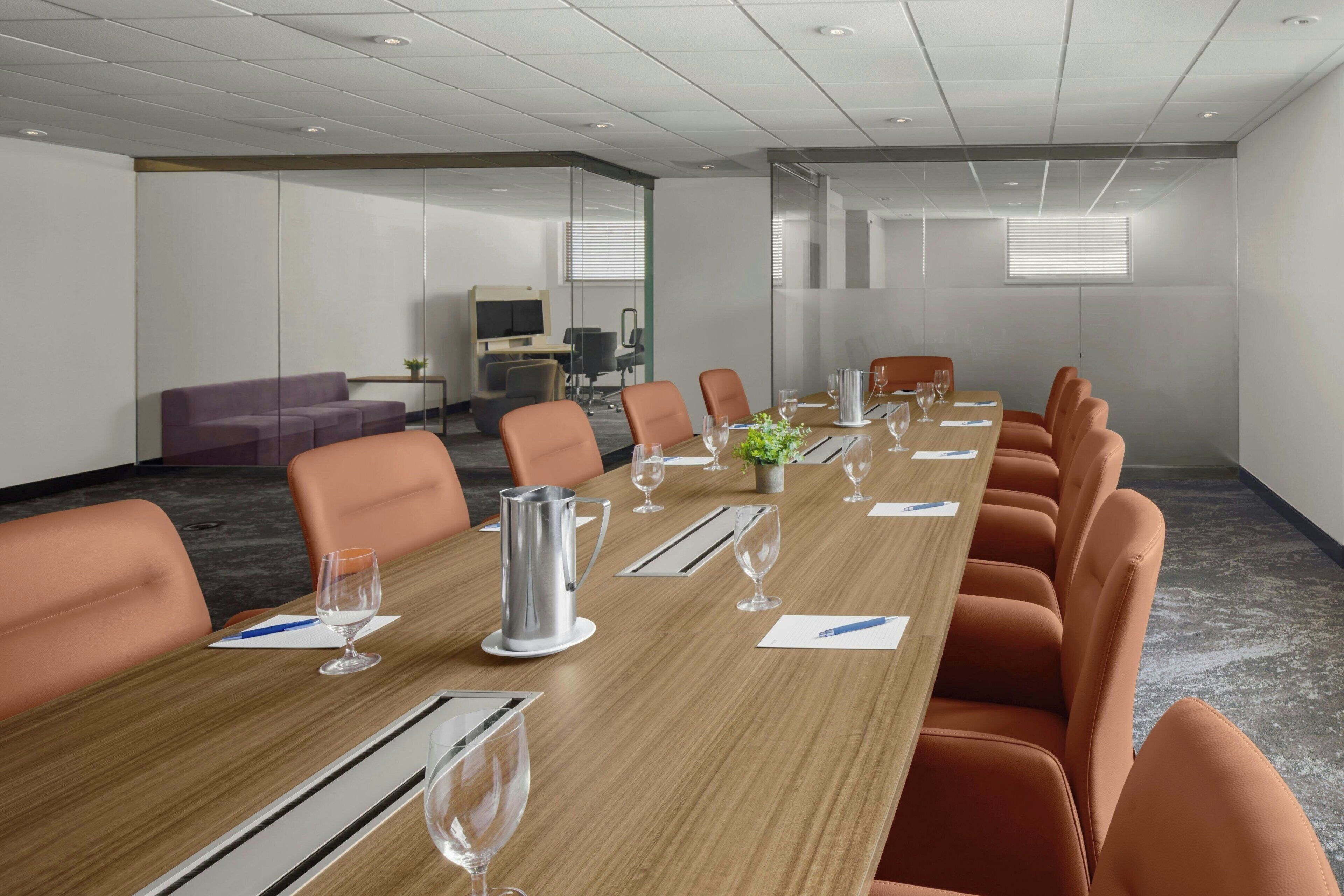 A conference room with a long table, orange chairs, and a coffee pot.