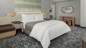 A hotel room with a bed, bedside tables, a sofa, a mirror, and a wall-mounted lamp.