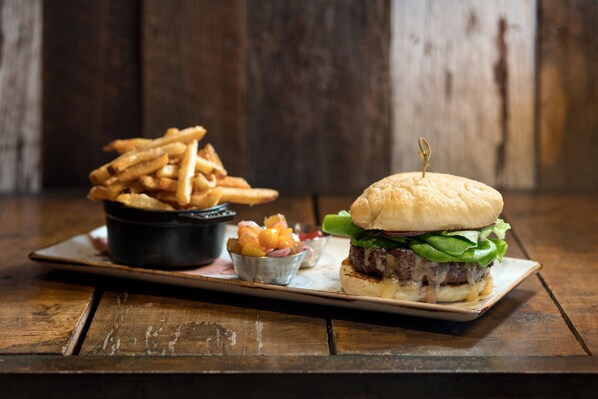 A burger with a bun, lettuce, and a toothpick, served with fries and a small bowl of pickles.