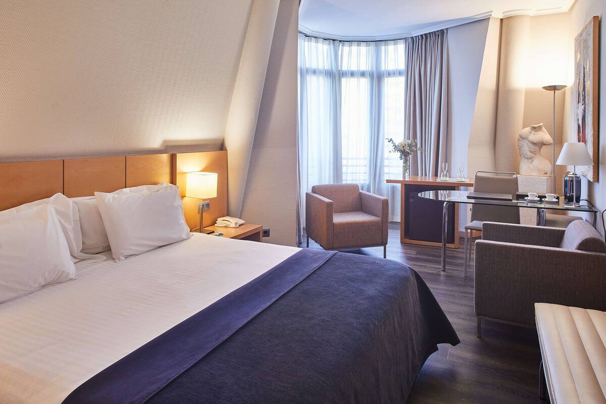 A hotel room with a large bed, a desk, a chair, and a sofa.