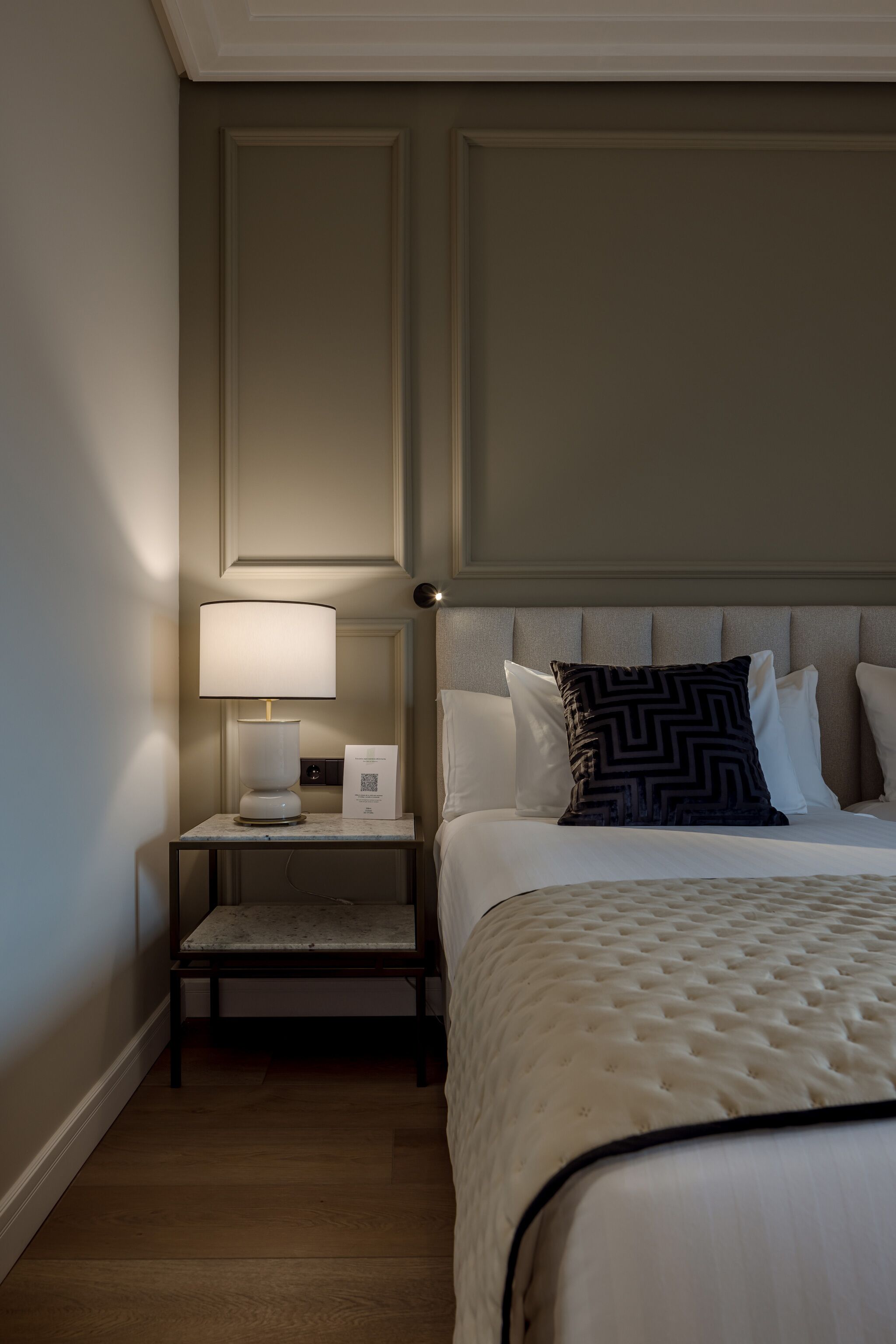 Una habitación de hotel con una cama bien hecha, una mesita de noche con una lámpara y una mesilla.