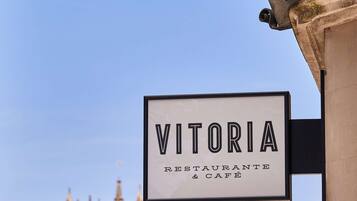 A sign for "Vitoria Restaurante & Cafe" with a historic building in the background.