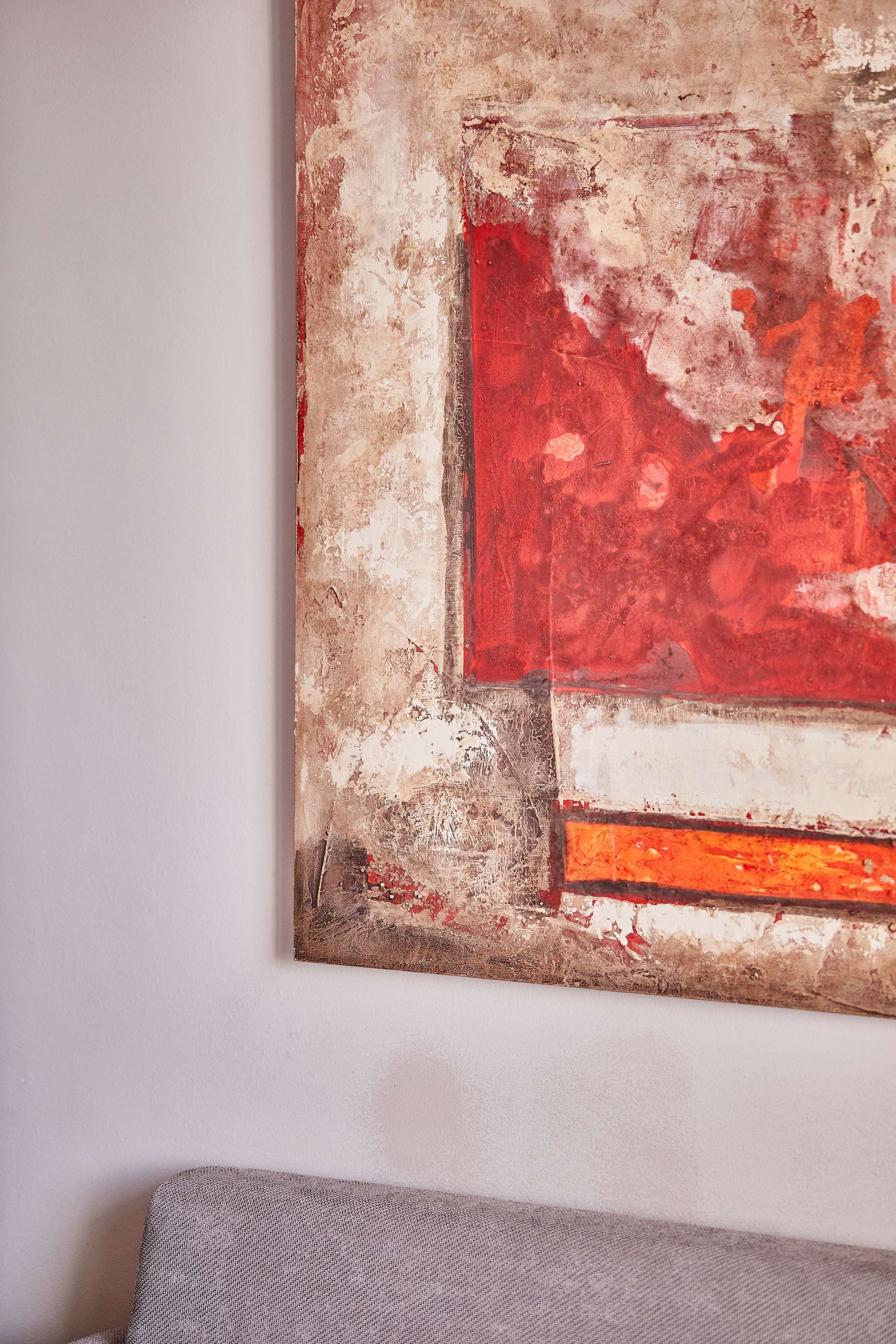 A textured abstract painting with red, white, and orange colors on a wall.